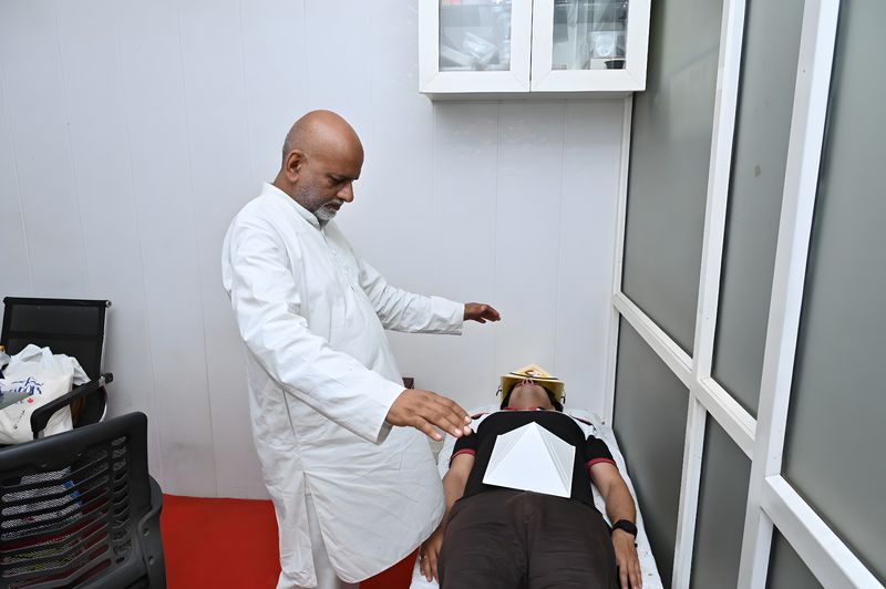 Sanjay Shrivastava holding both hands over a client wearing a pyramid cap