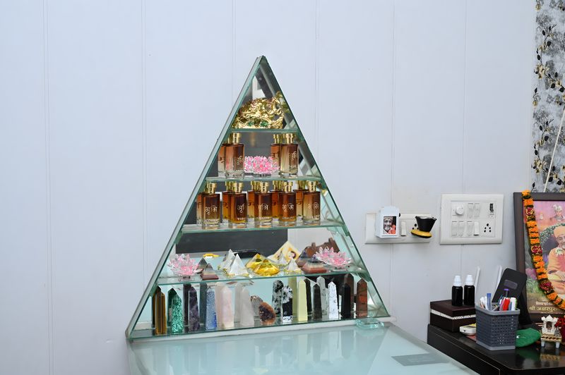 The triangular glass shelf of aroma oils, crystal pyramids and crystal towers beside his desk